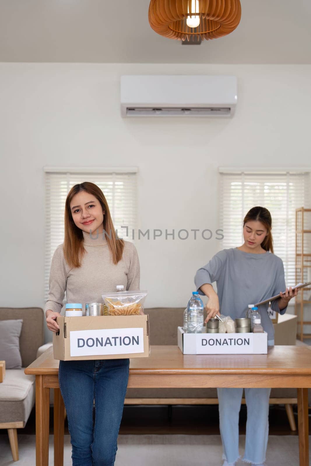 Donation and two woman volunteer asian of happy packing food in box at home. Charity by nateemee