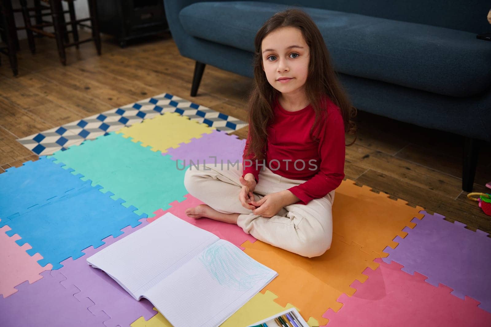 Adorable elementary age child, little school girl at home, doing homework, writing on copy book, smiling looking at camera by artgf