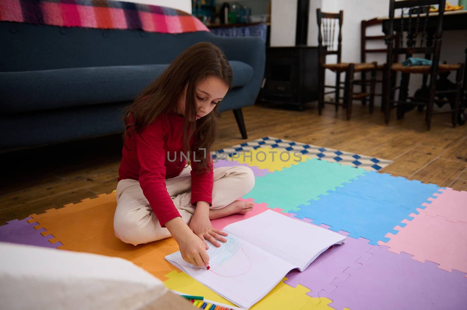 Lovely little child girl sitting on a colorful puzzle carpet, studying from home, doing homework. People. Kids. Education concept by artgf