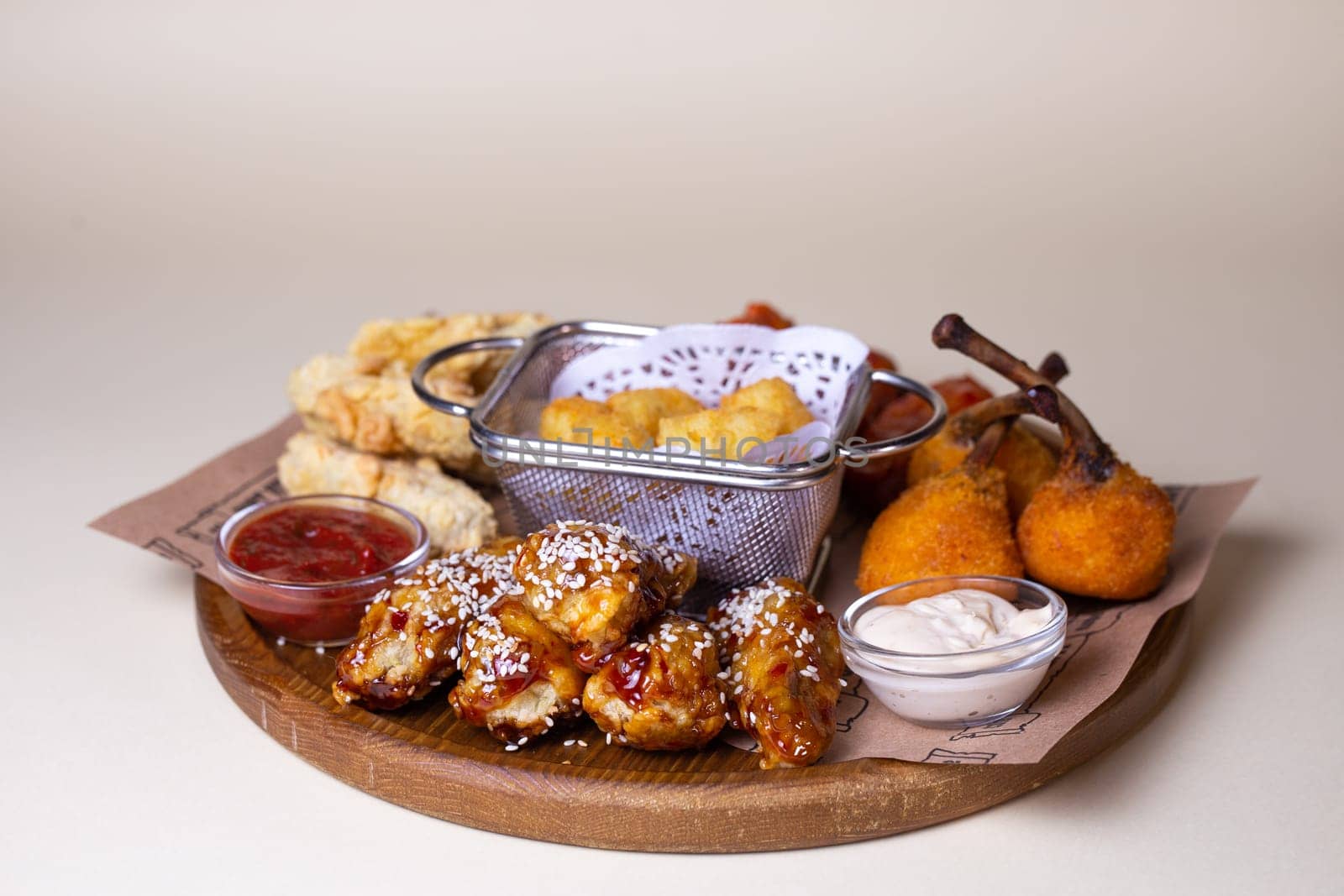 A variety of fried chicken wings, potato balls, and cheese sticks with dipping sauces on a wooden platter.