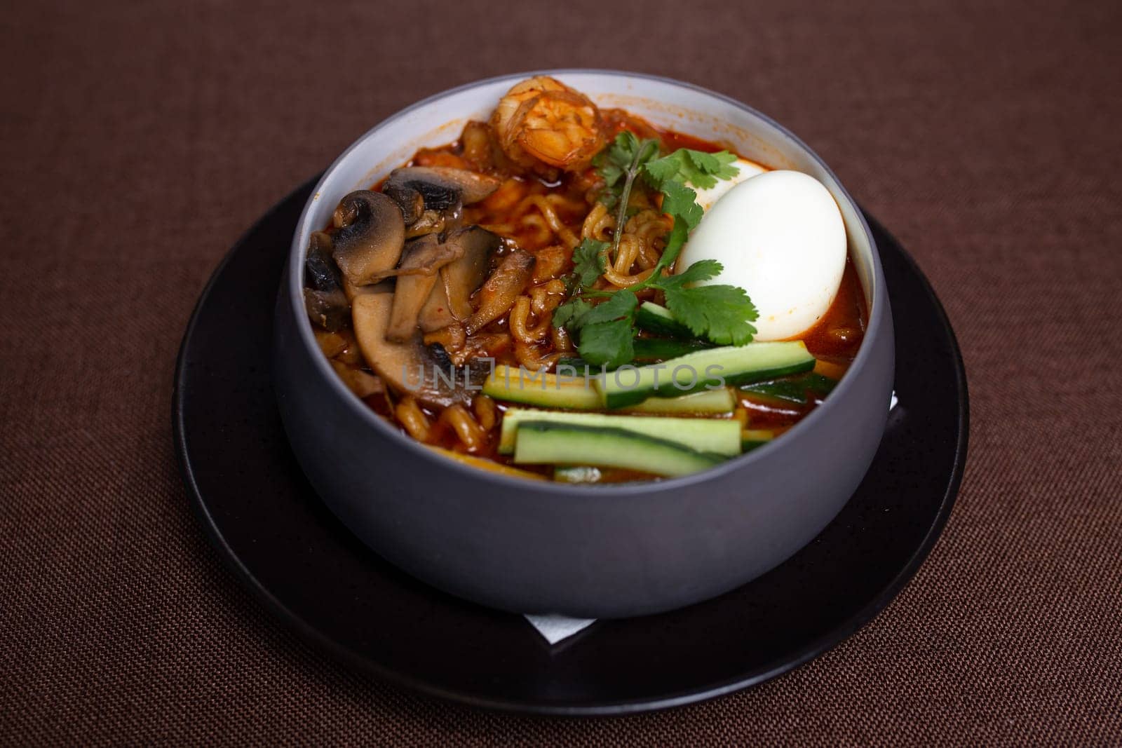 Bowl of spicy Korean ramen with mushrooms, egg, cucumber, and cilantro. by Pukhovskiy