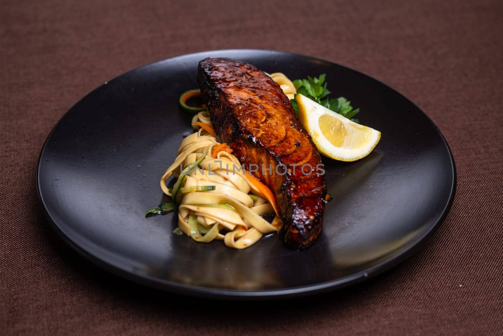 A mouthwatering and nutritious dish featuring grilled salmon, lemon, and fresh vegetables on a sleek black plate.