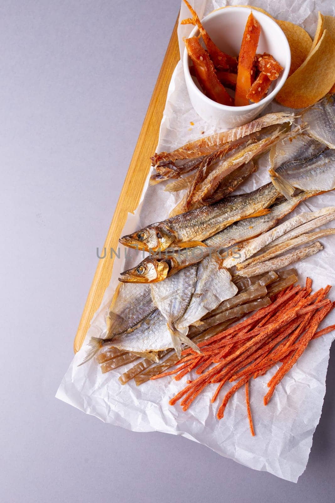 Assorted dried fish, fish skin, and fruit snacks on white paper on a wooden table, creating a vibrant culinary display.