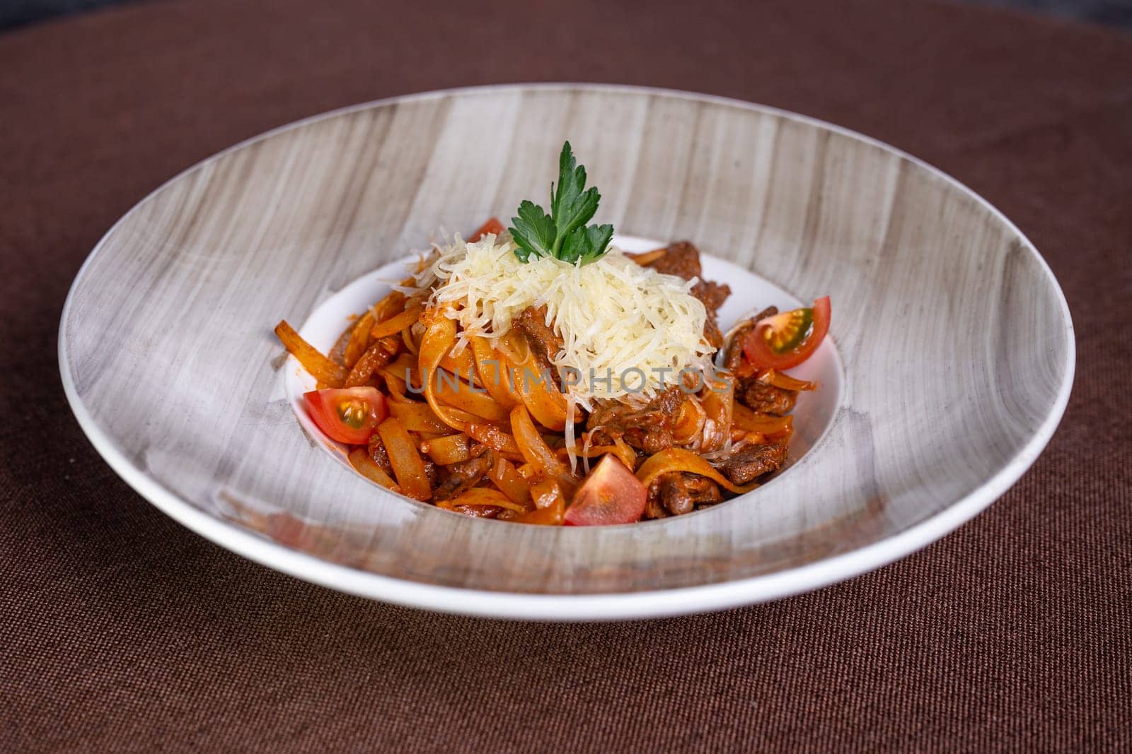 Top view of a delicious plate of beef stew with pasta, tomatoes, and cheese topping, perfect for lunch or dinner.