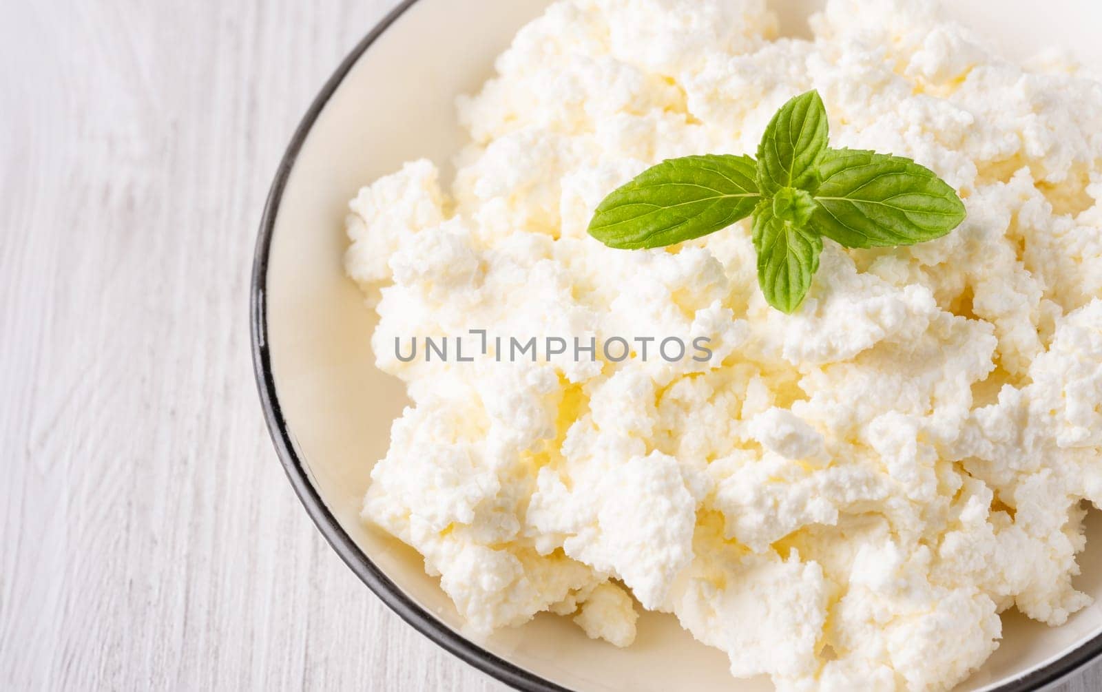 Cottage cheese in a plate on a white table, with copy space for text.