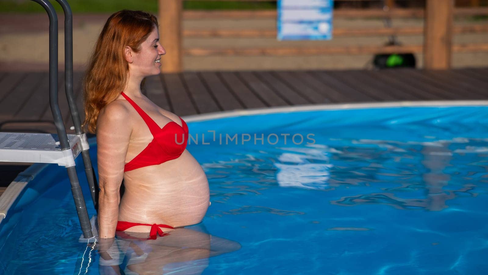 Pregnant red-haired woman in the pool in a red bikini