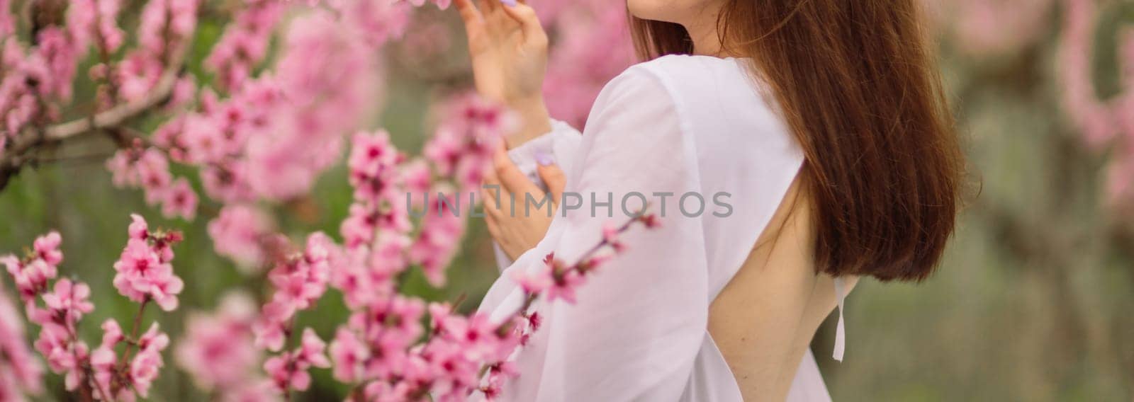A girl is walking through a field of pink peach flowers. She is wearing a white dress and carrying a basket. The scene is peaceful and serene, with the pink flowers creating a beautiful by Matiunina