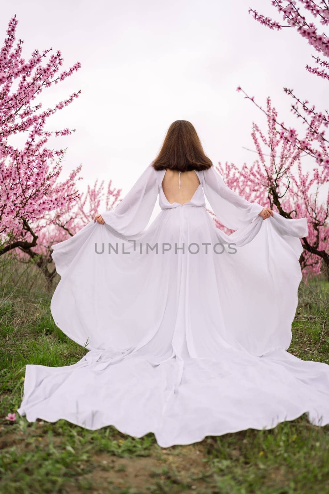 A woman in a white dress is walking through a field of pink flowers. She is holding her arms up in the air, as if she is celebrating or expressing joy. The scene is serene and peaceful. by Matiunina