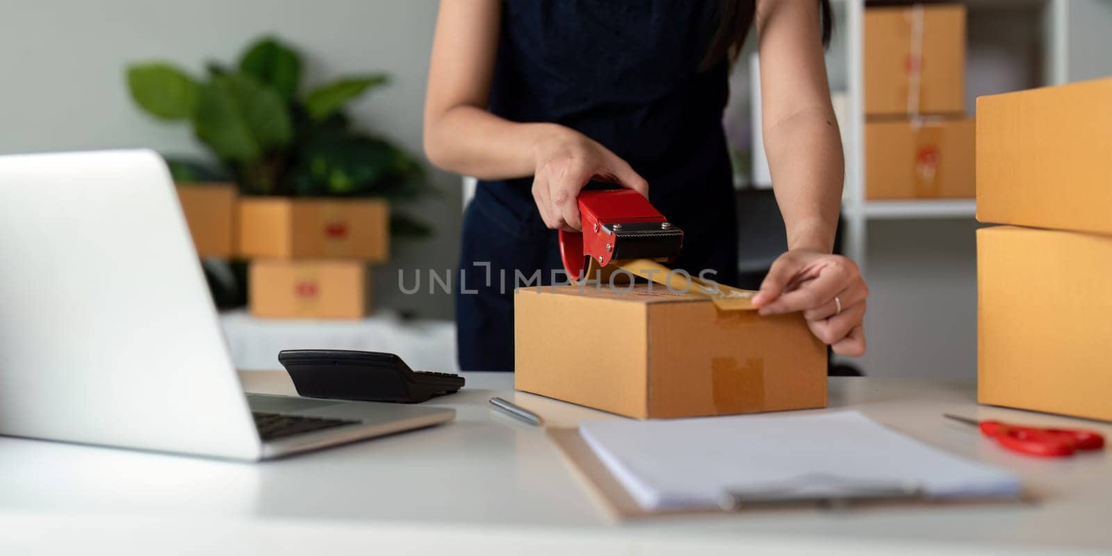 Woman use scotch tape to attach parcel boxes to prepare goods for the process of packaging at home, shipping, online sale internet marketing ecommerce concept startup business idea by nateemee