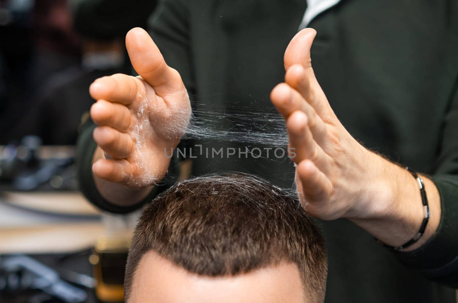 Hairdresser adjusts freshly cut hair of client in barbershop closeup. Careful stylist tousles haircut serving man in grooming salon