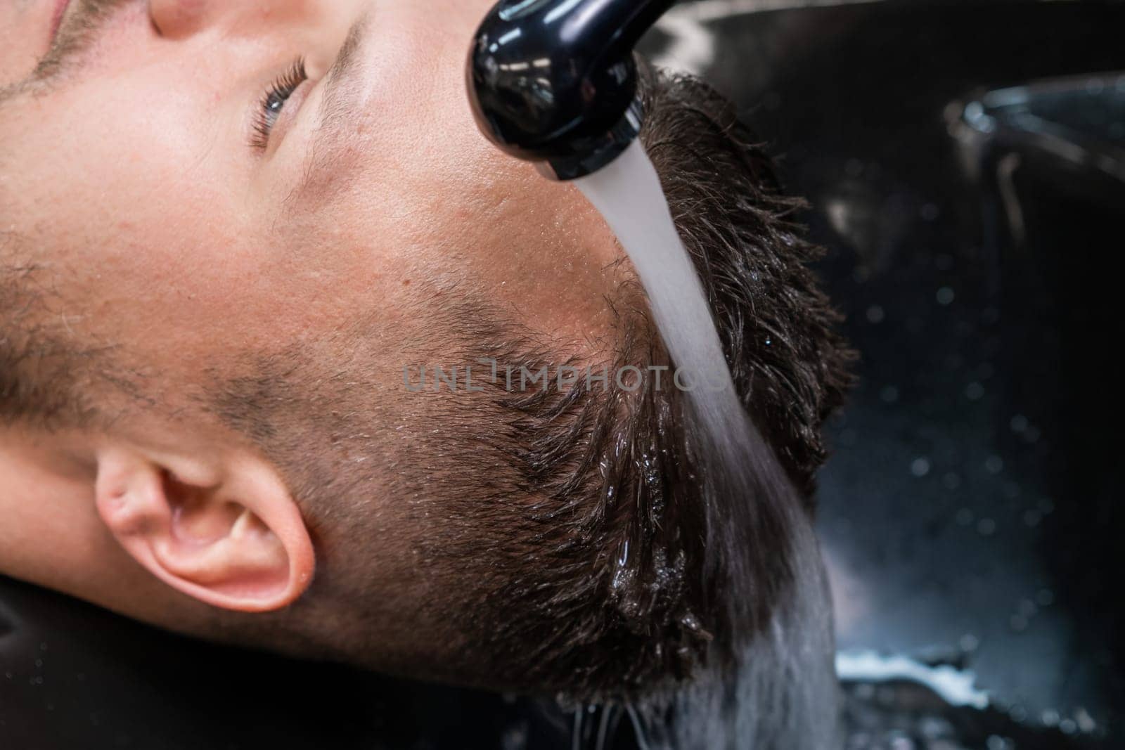 Hairdresser washes man hair from shampoo with warm water by vladimka