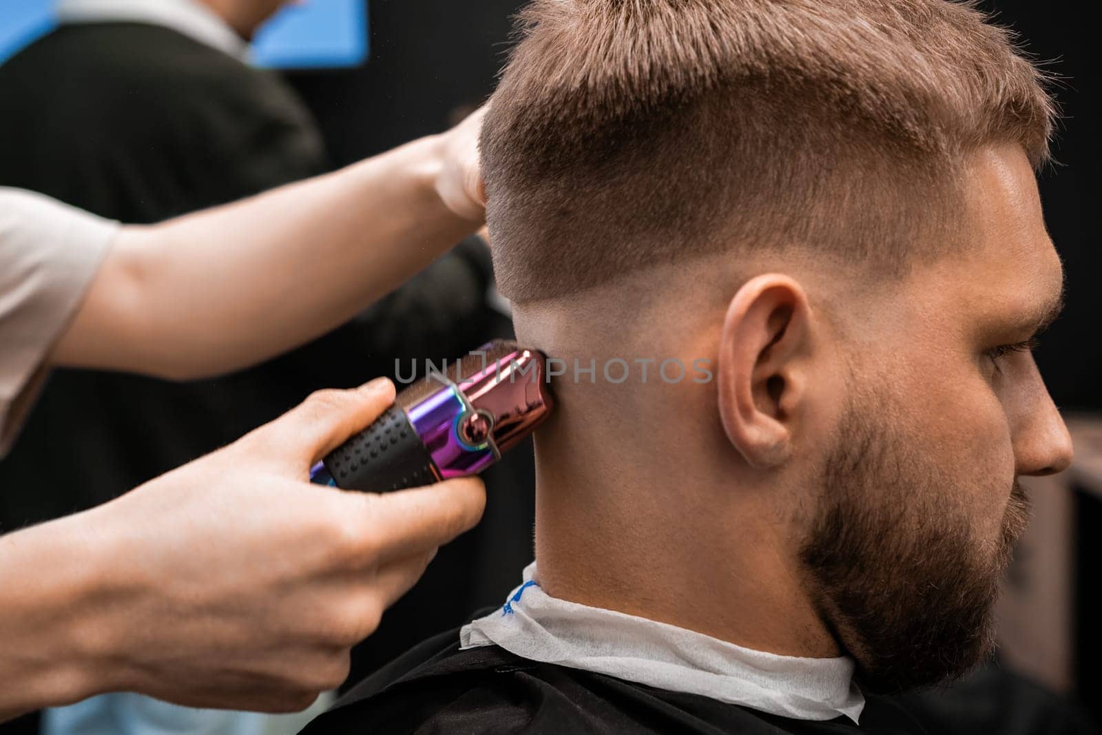 Barber shaves client nape with electric shaver in barbershop by vladimka