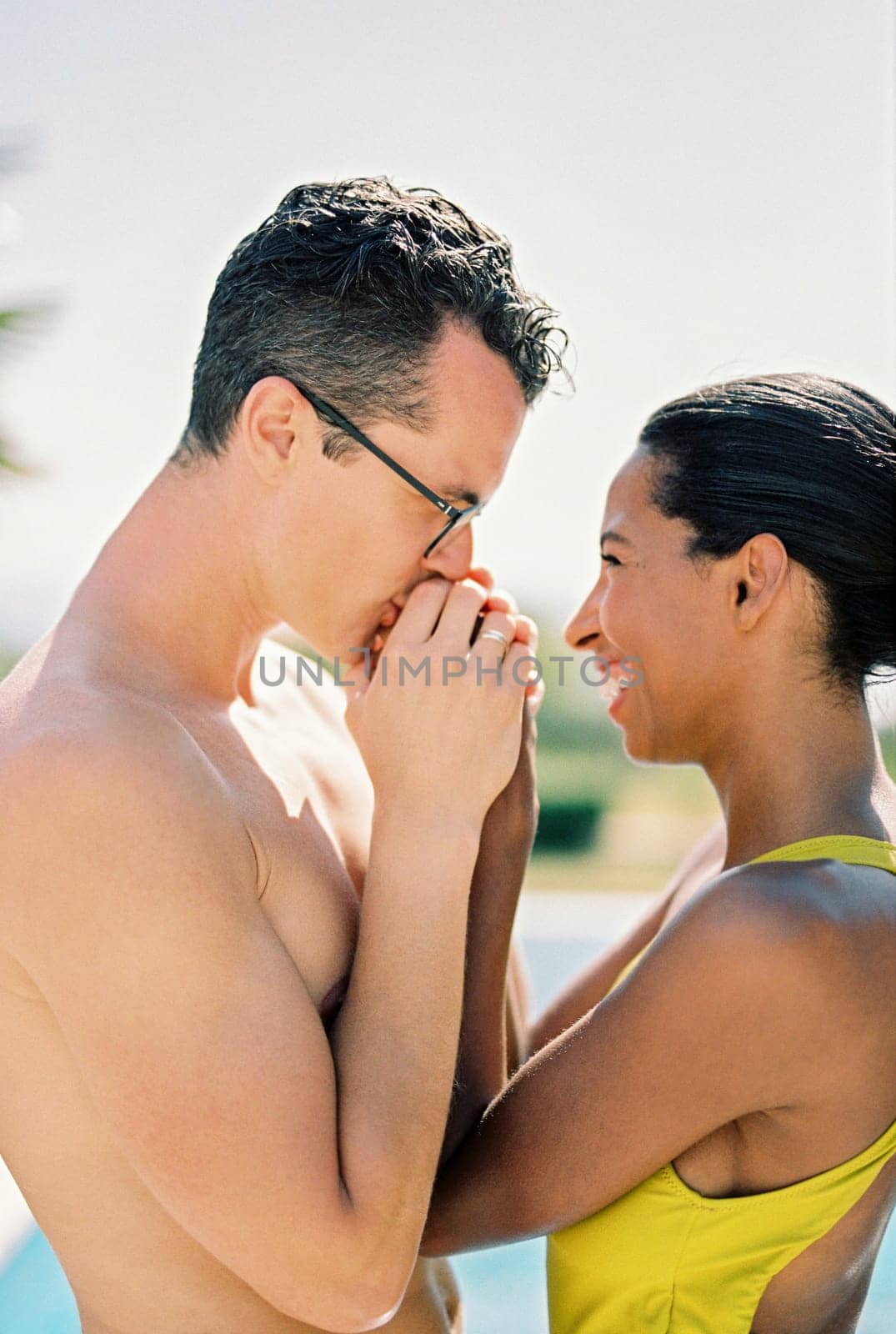 Husband kisses the hands of his smiling wife while standing near the pool. Close-up. High quality photo