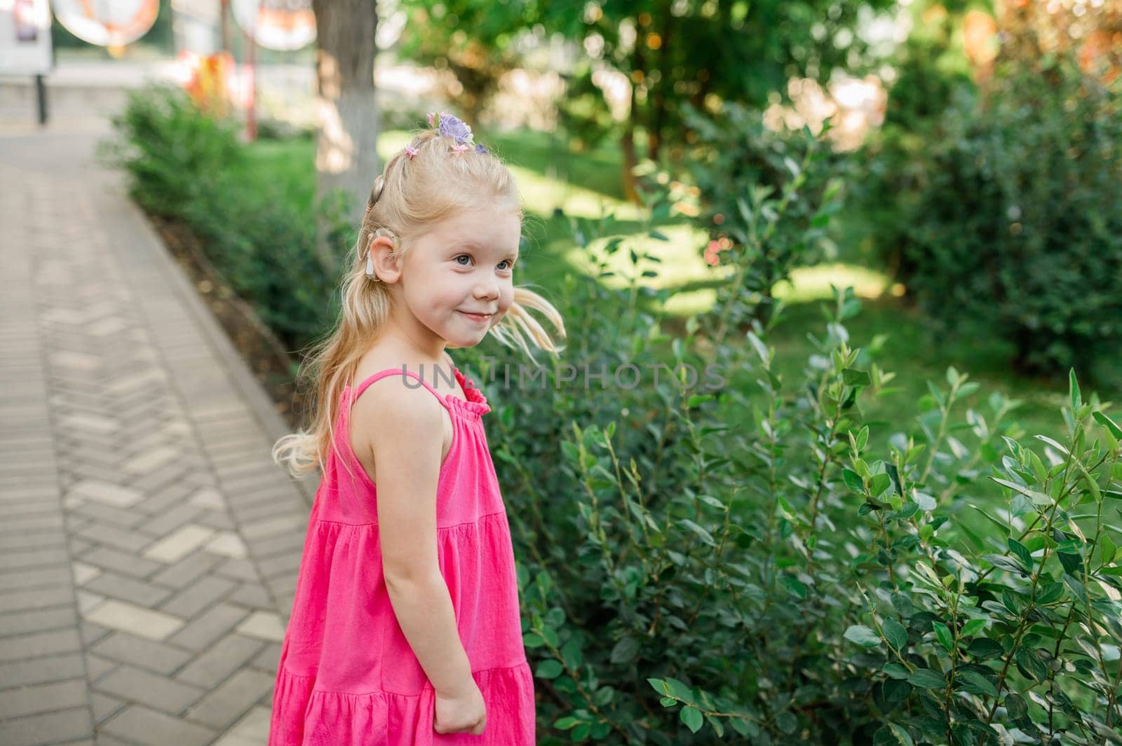 Child girl walks and have fun outdoor with cochlear implant on the head. Hearing aid and treatment concept. Inclusion and disability. Copy space and empty place for text. by Satura86