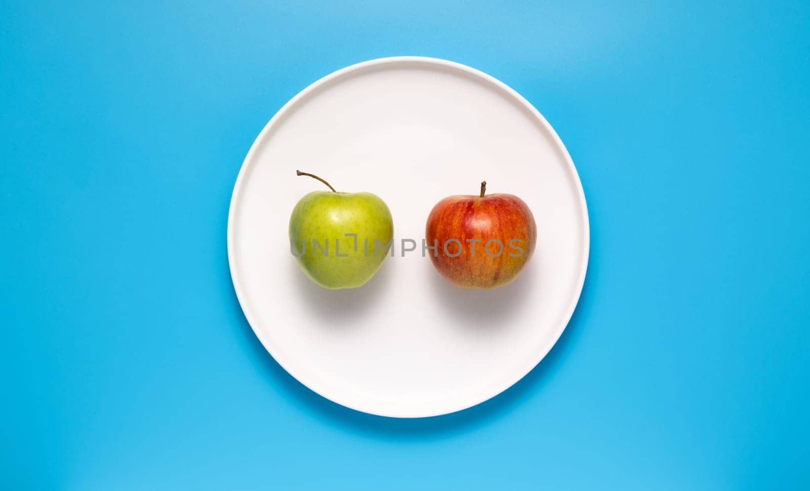Red and green apple on a white plate on a blue background.