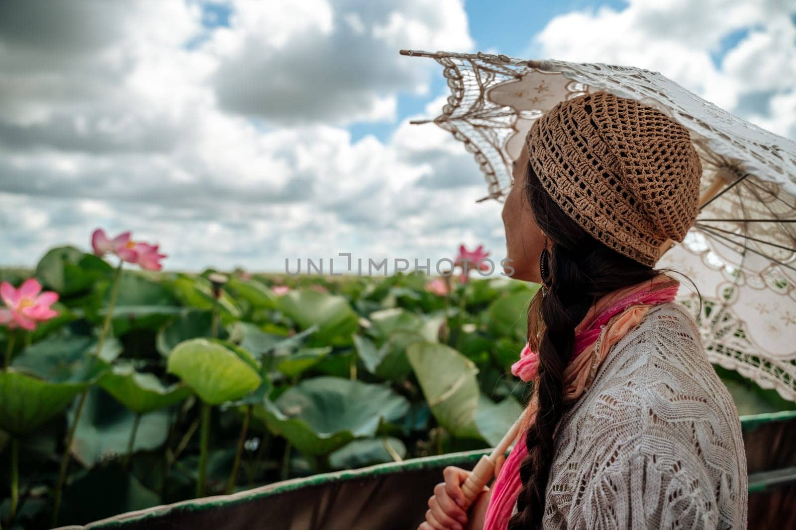 A woman wearing a hat and holding an umbrella is looking at a field of pink flowers. The scene is peaceful and serene, with the woman taking in the beauty of the flowers. by Matiunina