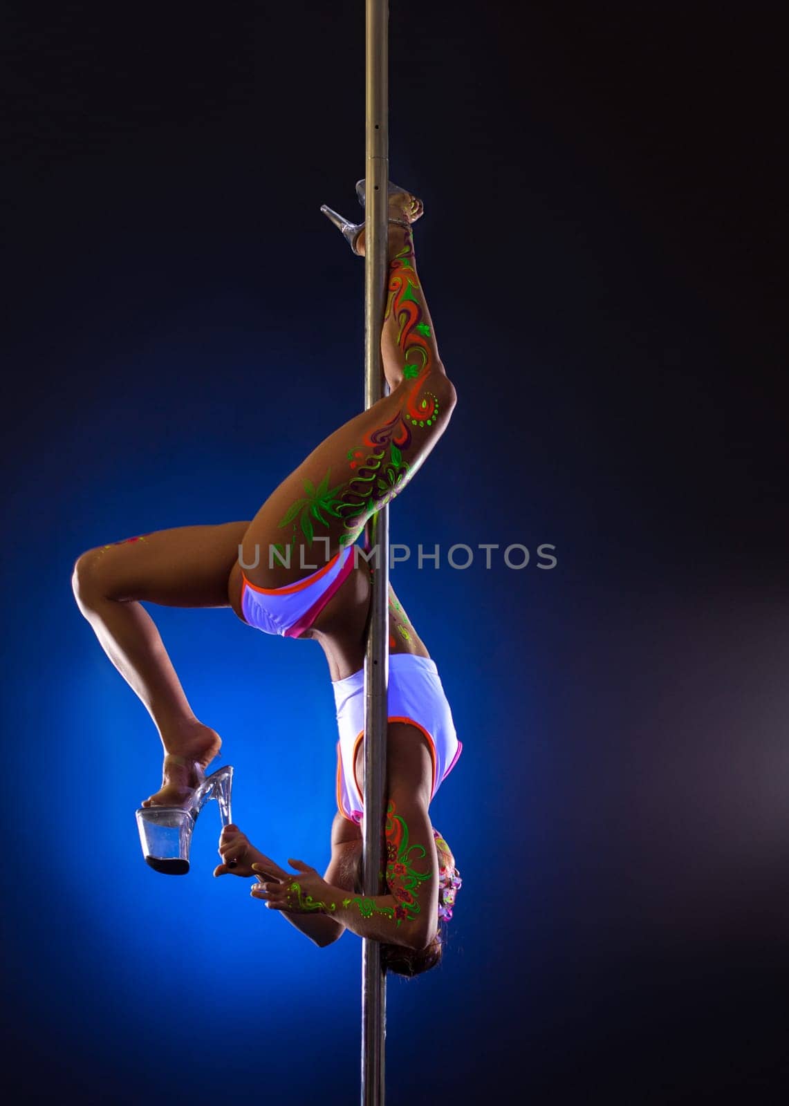 Flexible female dancer hangs upside down on pole