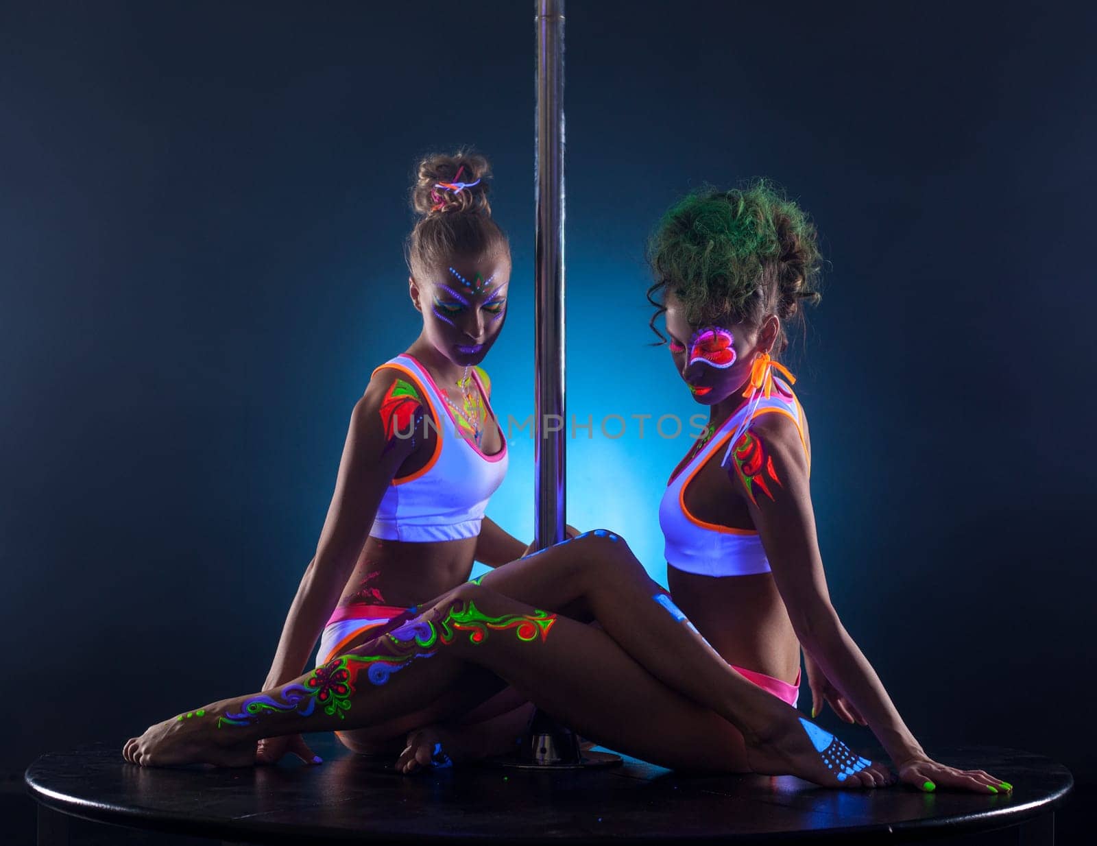 Sexy female dancers posing sitting together near pole