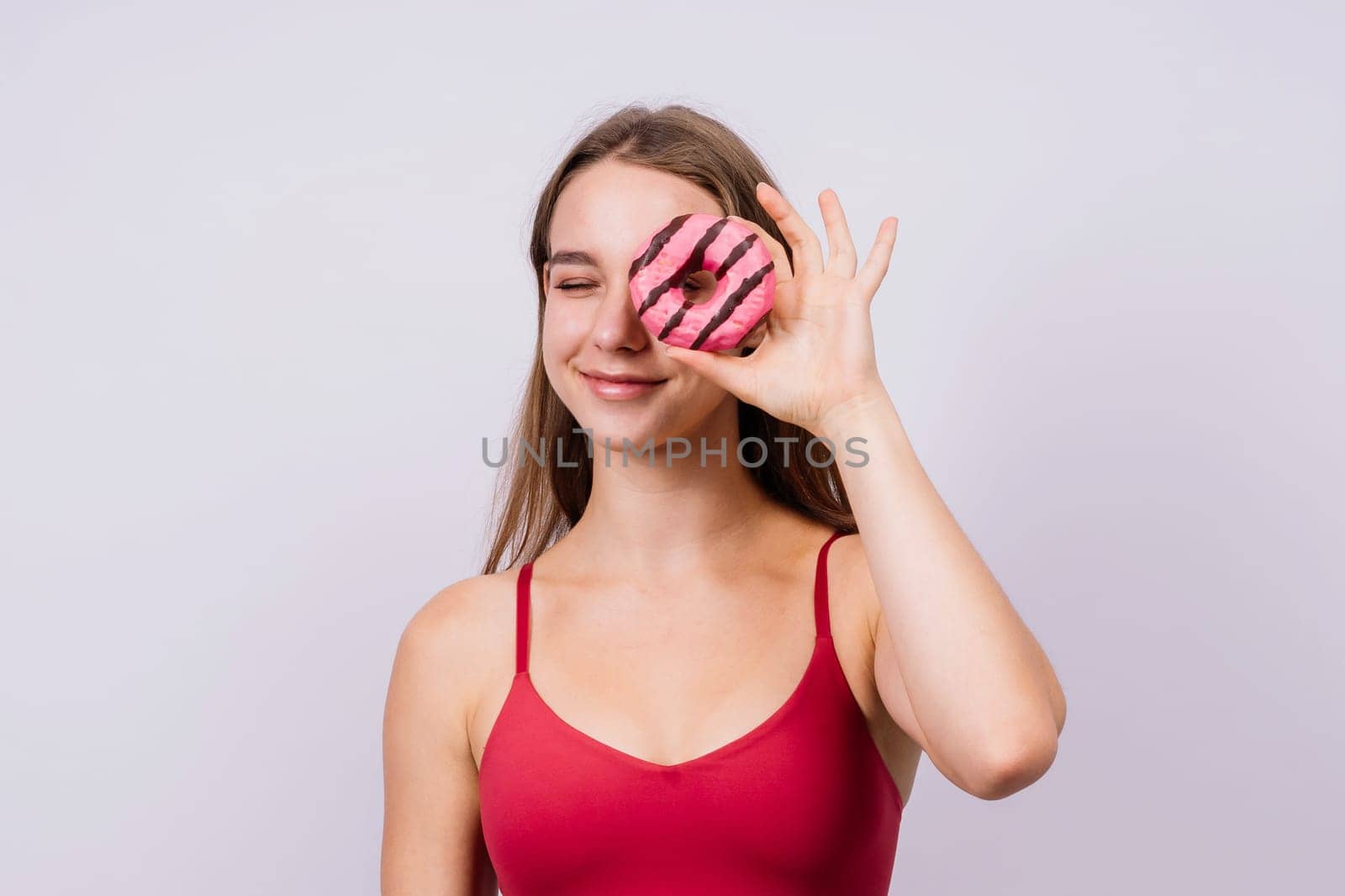 Young cute sport woman eating a donut cake in studio background by Zelenin