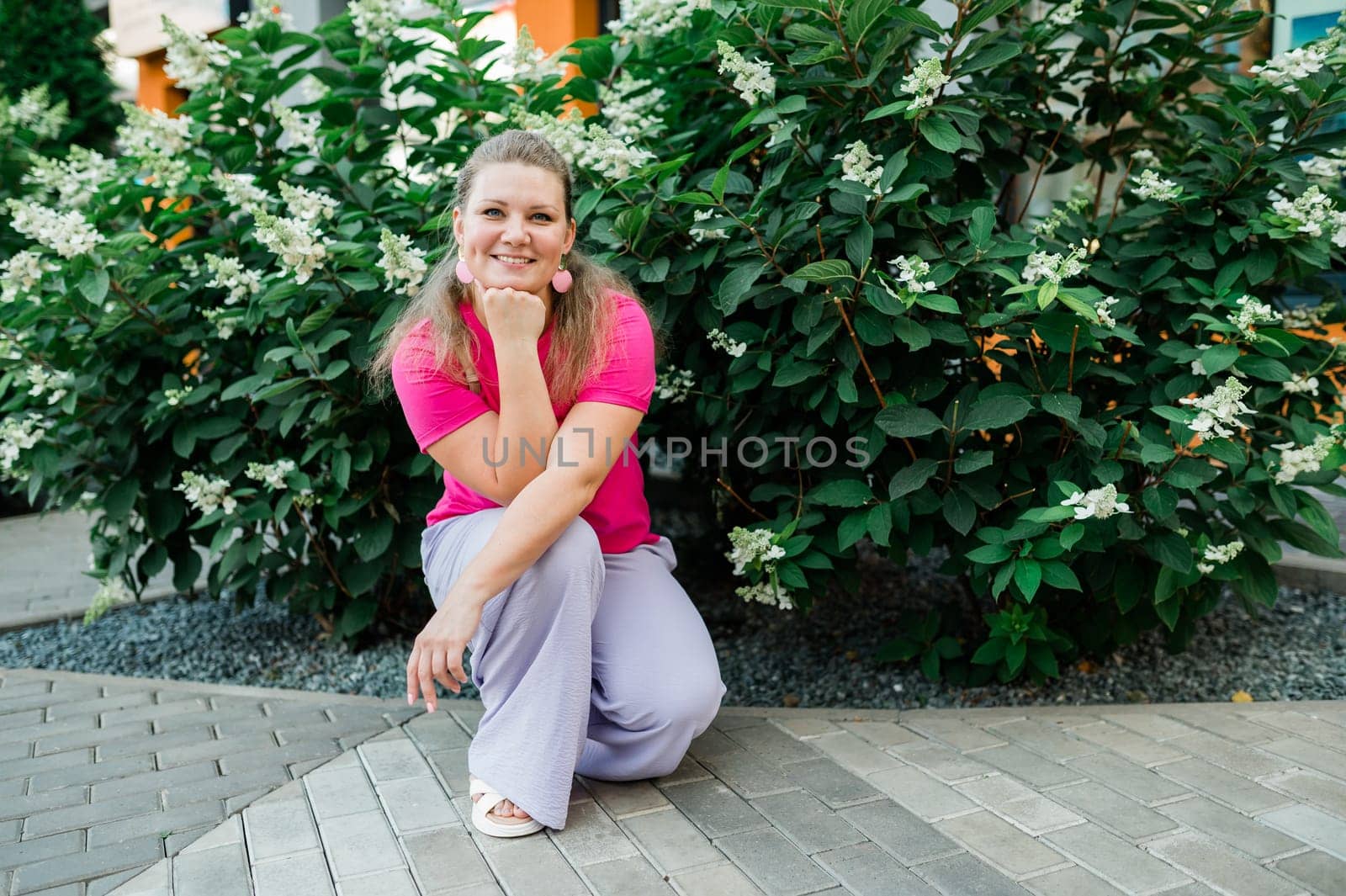 Portrait of beautiful smiling millennial woman wearing stylish pink t shirt looking at camera standing in green park. Positive lifestyle, natural beauty concept. Copy space.