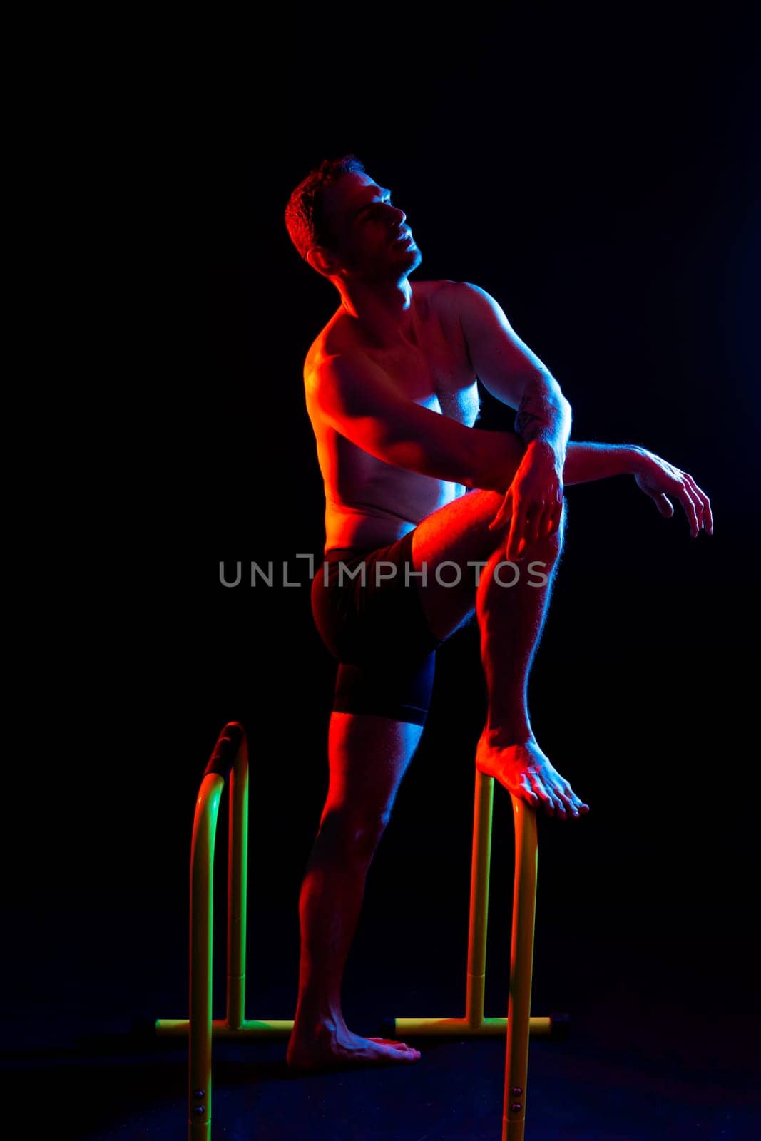 Front and side view photo of strong young man exercising on parallel bars in studio.