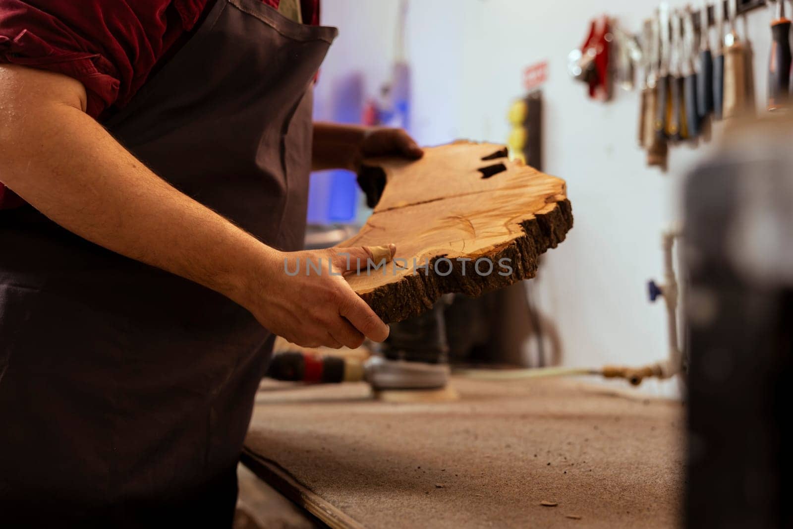 Carpenter holding timber block, doing quality assurance on it before starting furniture assembling in workshop, close up shot. Manufacturer in joinery preparing piece of wood for carving