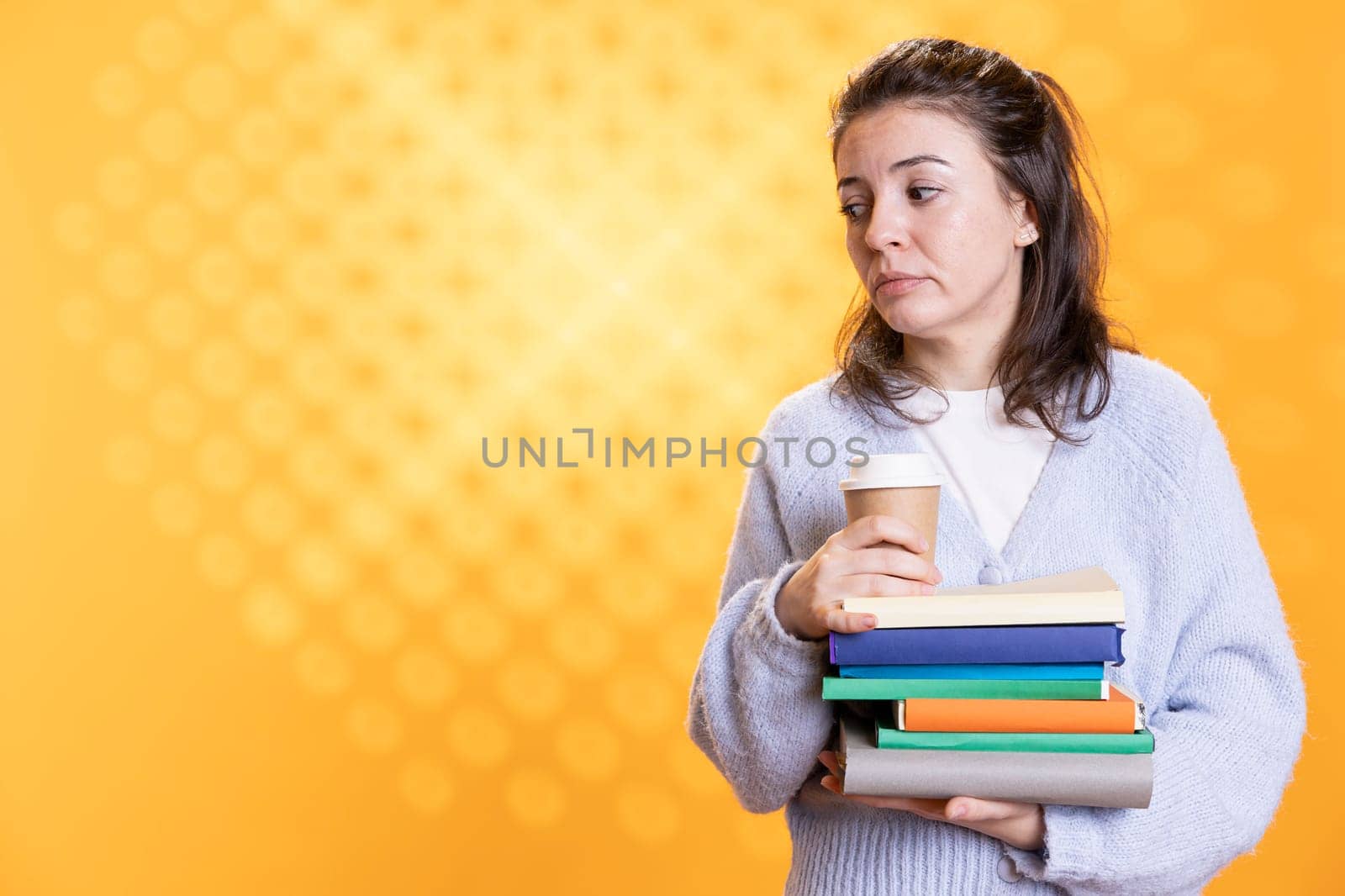 Portrait of woman with stack of books in hands holding disposable cup of coffee, isolated over studio background. Bookworm holding pile of novels and caffeinated drink early in the morning