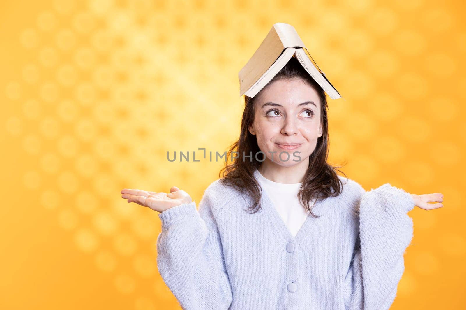 Woman with opened book on head acting zany, portraying having fun concept, isolated over studio background. Bookworm wearing novel and as hat, enjoying life, clowning around, feeling excited