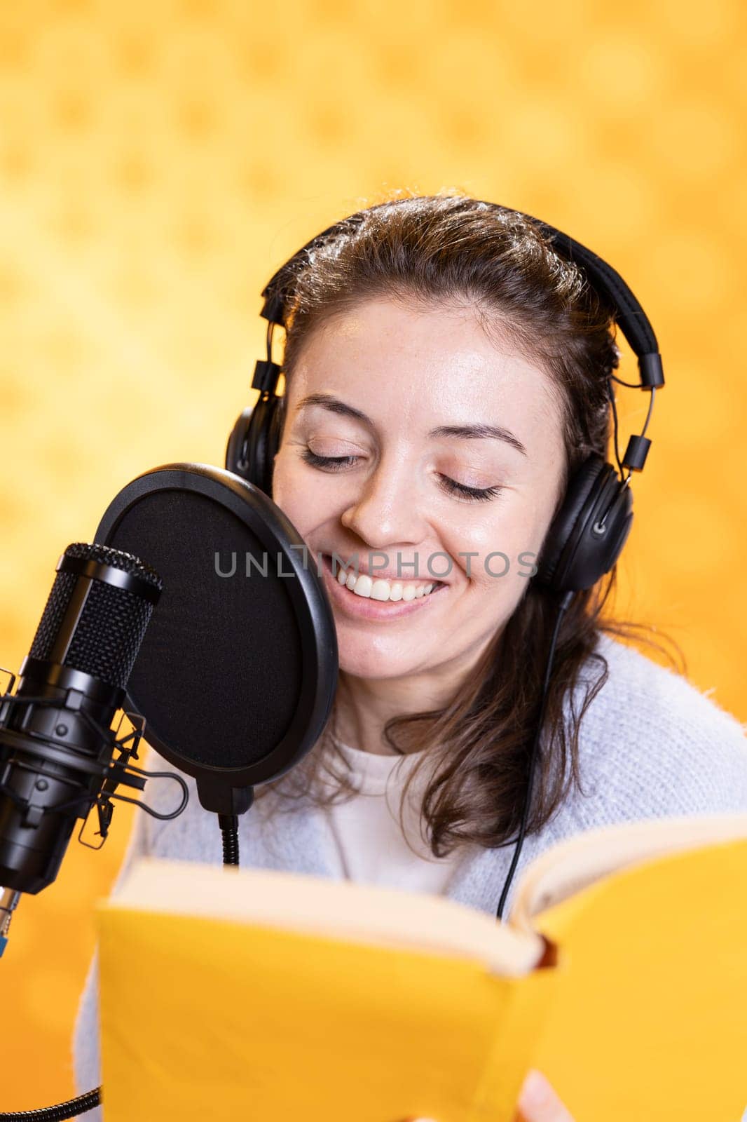Happy narrator wearing headphones reading aloud from book into mic by DCStudio