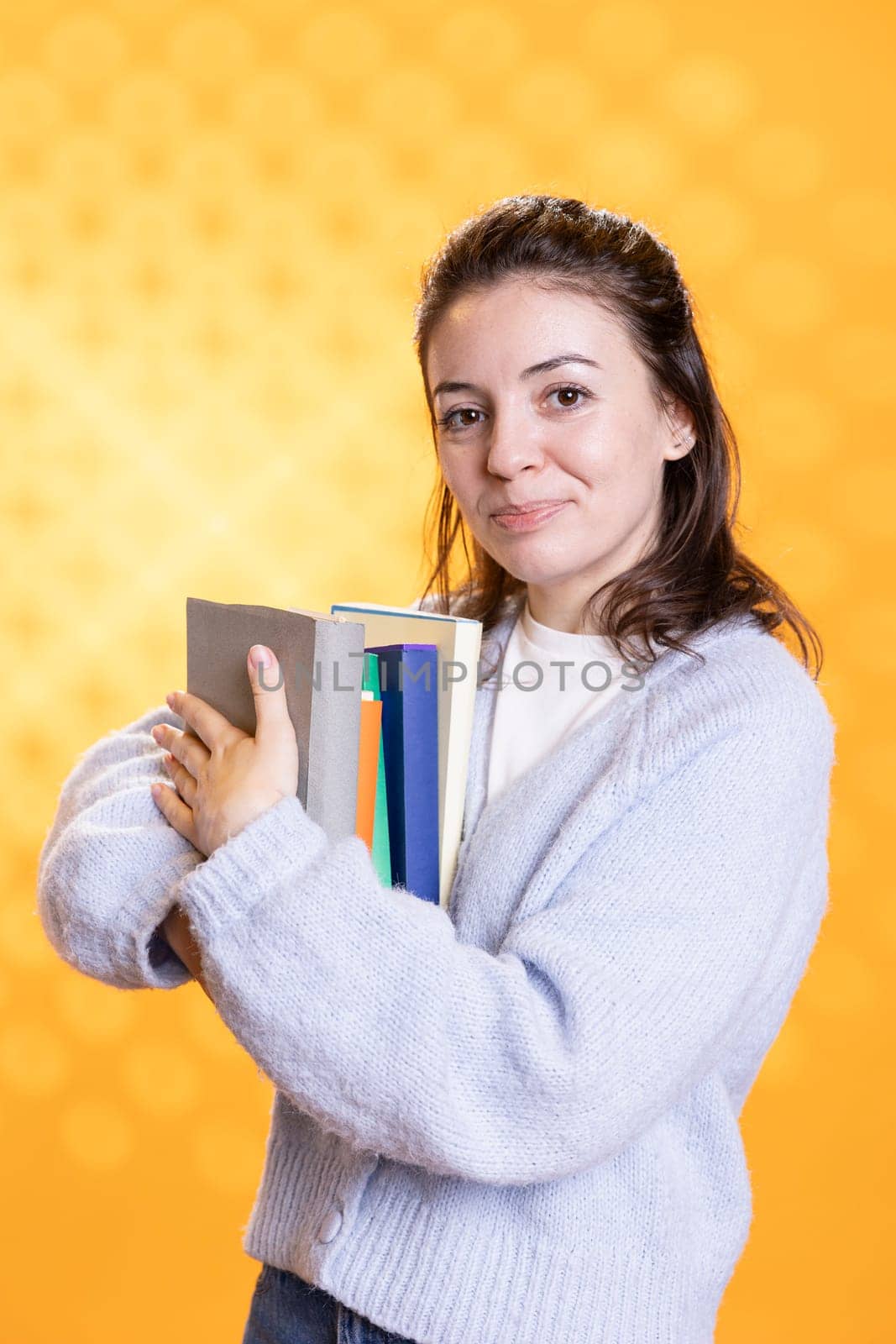 Portrait of happy woman hugging stack of textbooks, gathering information for school exam, isolated over studio background. Jolly person holding pile of books, preparing for university assessment