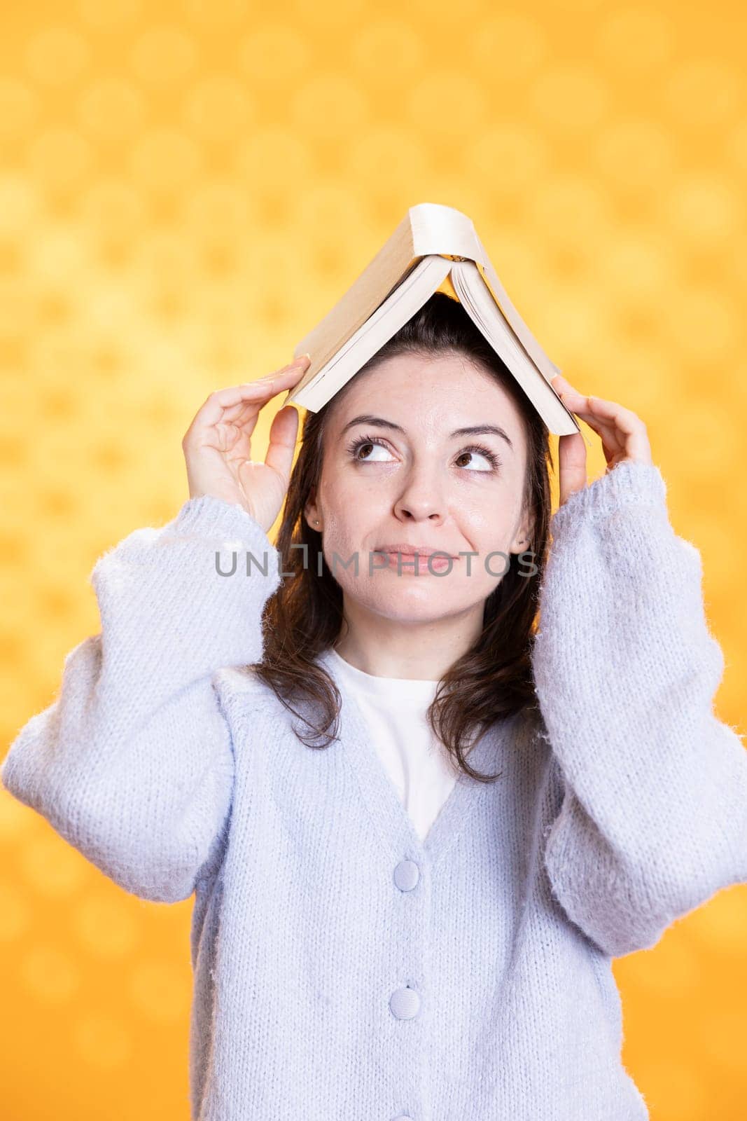 Portrait of joyous woman placing book on head, acting zany, studio background by DCStudio