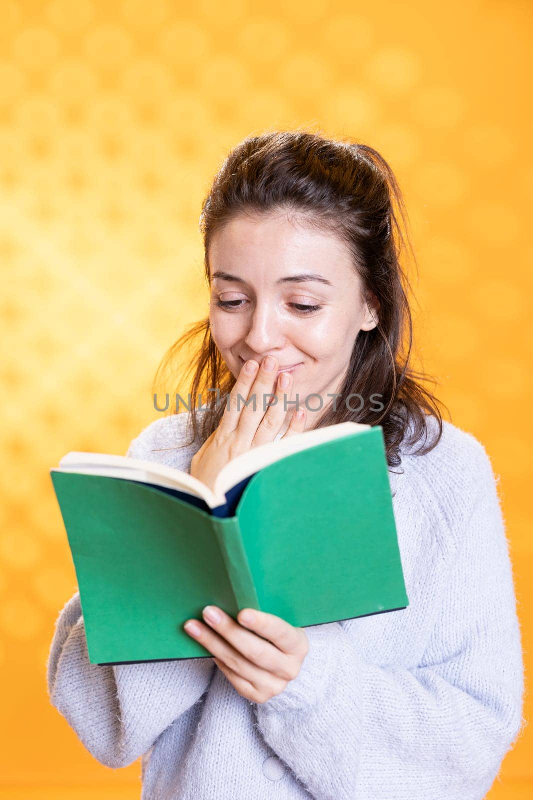 Woman amused by funny book, conveying joy of reading concept, isolated over studio background. Geek enjoying comical novel, giggling at jokes, showing appreciation for literature