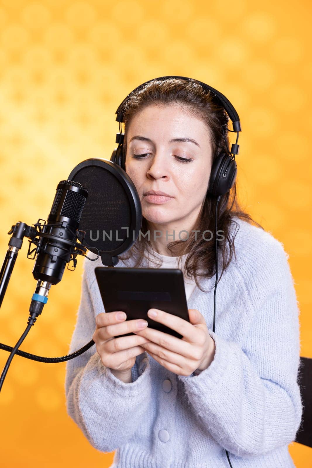 Woman doing voiceover word for word reading of ebook on ereader to produce audiobook. Narrator using storytelling skills while reading text from tablet, recording novel, studio background