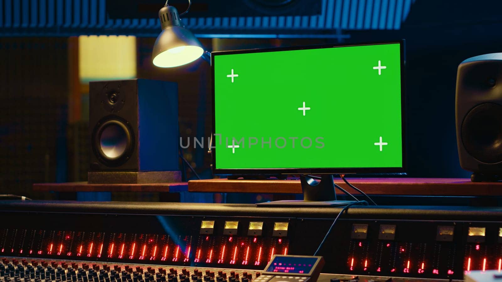 Empty professional recording studio control room with greenscreen on display, editing and processing tracks. Motorized faders, buttons and sliders operated for mix and master techniques. Camera A.