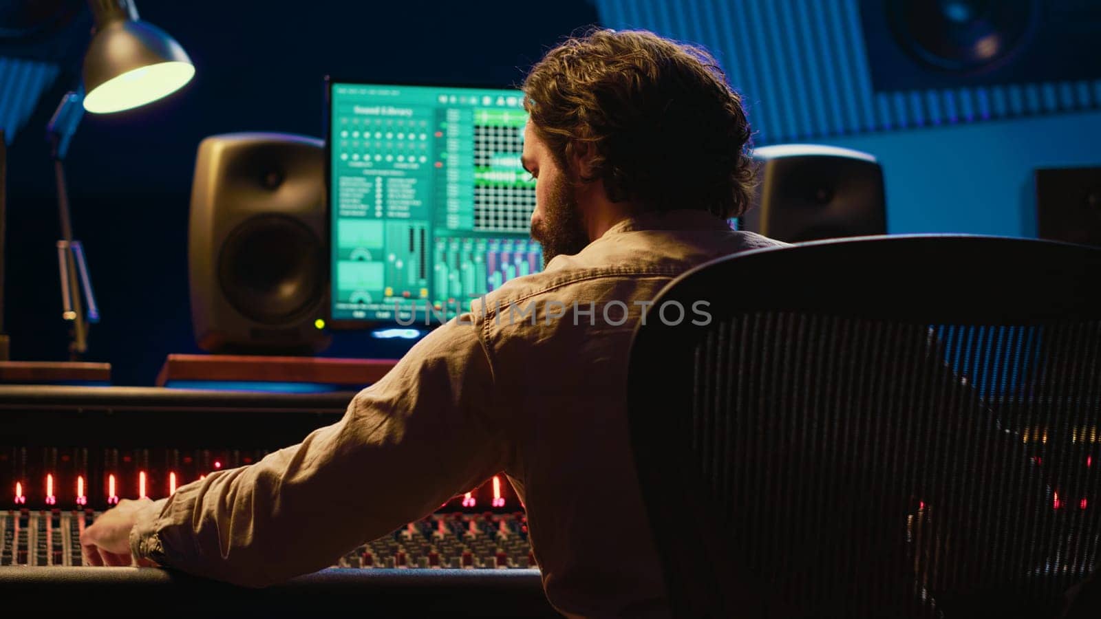 Sound designer mixing and mastering tracks on audio console in control room, using daw software on computer and editing files. Technician creating new music in professional studio. Camera A.
