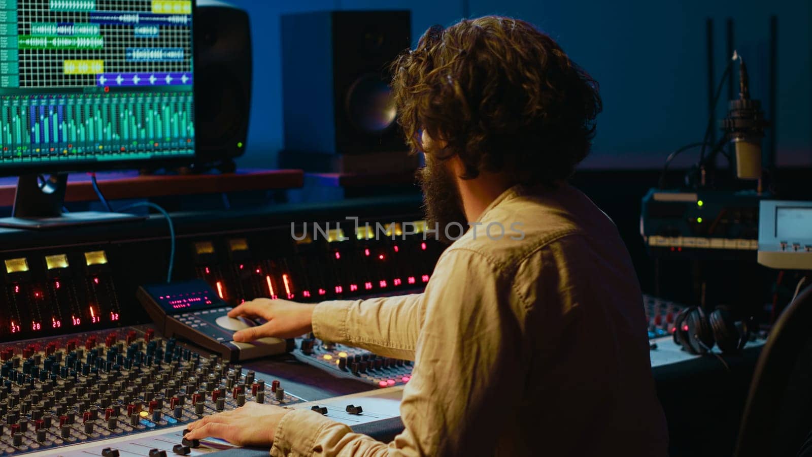 Music producer editing tracks with mixing console and audio software in studio, pressing key buttons and twisting knobs in control room. Sound engineer producing tunes and adjusting volume. Camera A.