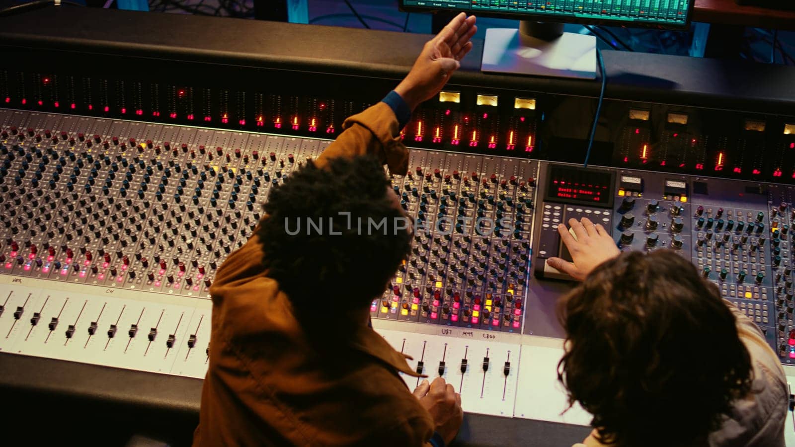 Music production team examining volume levels on audio software, using mixing and mastering techniques to create a hit song. Musician and sound designer work on editing recorded tracks. Camera B.