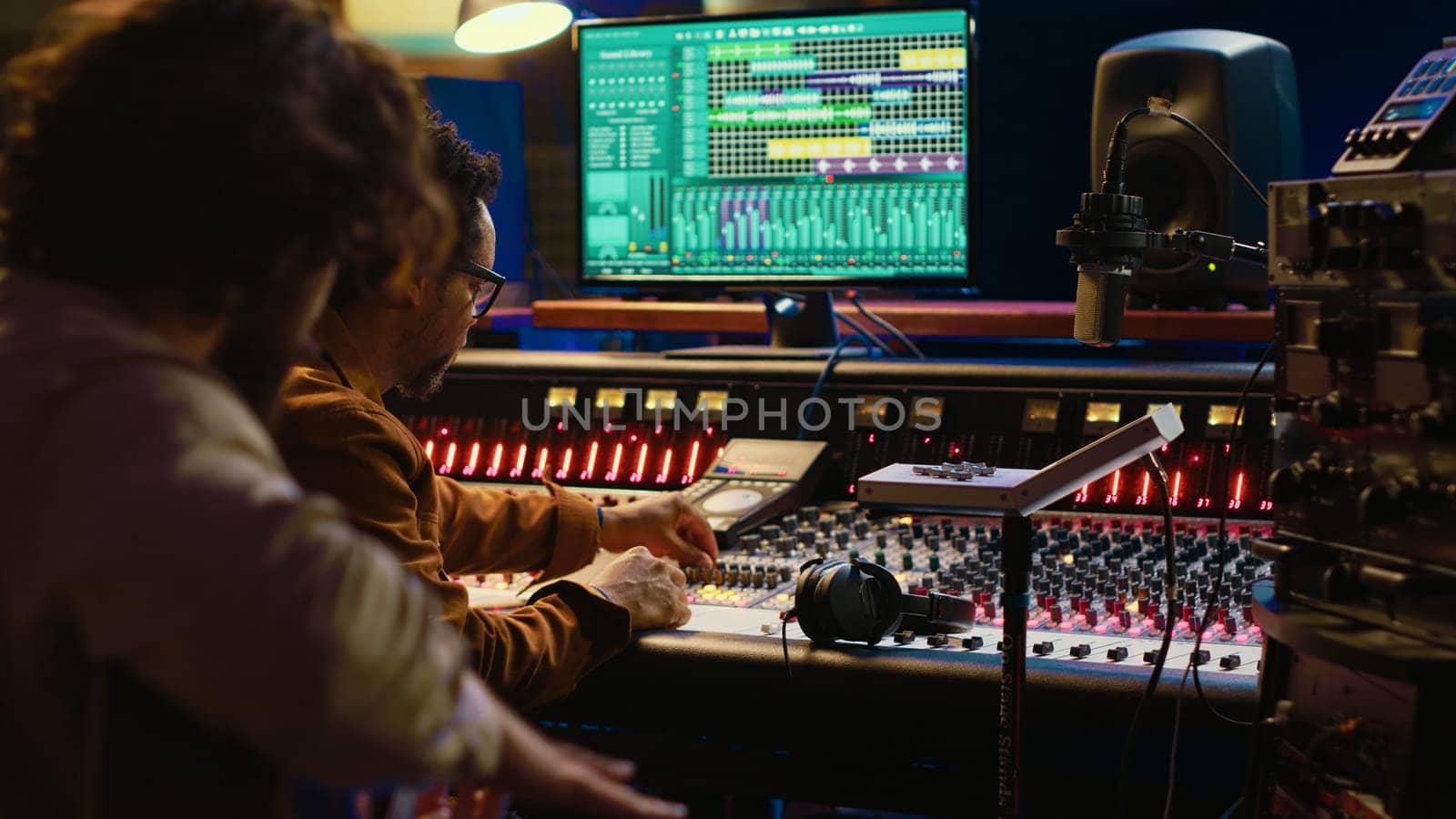 Guitarist recording his electro acoustic instrument and song in studio, producing new music with a sound engineer in control room. Skilled musician songwriter recording tracks. Camera A.