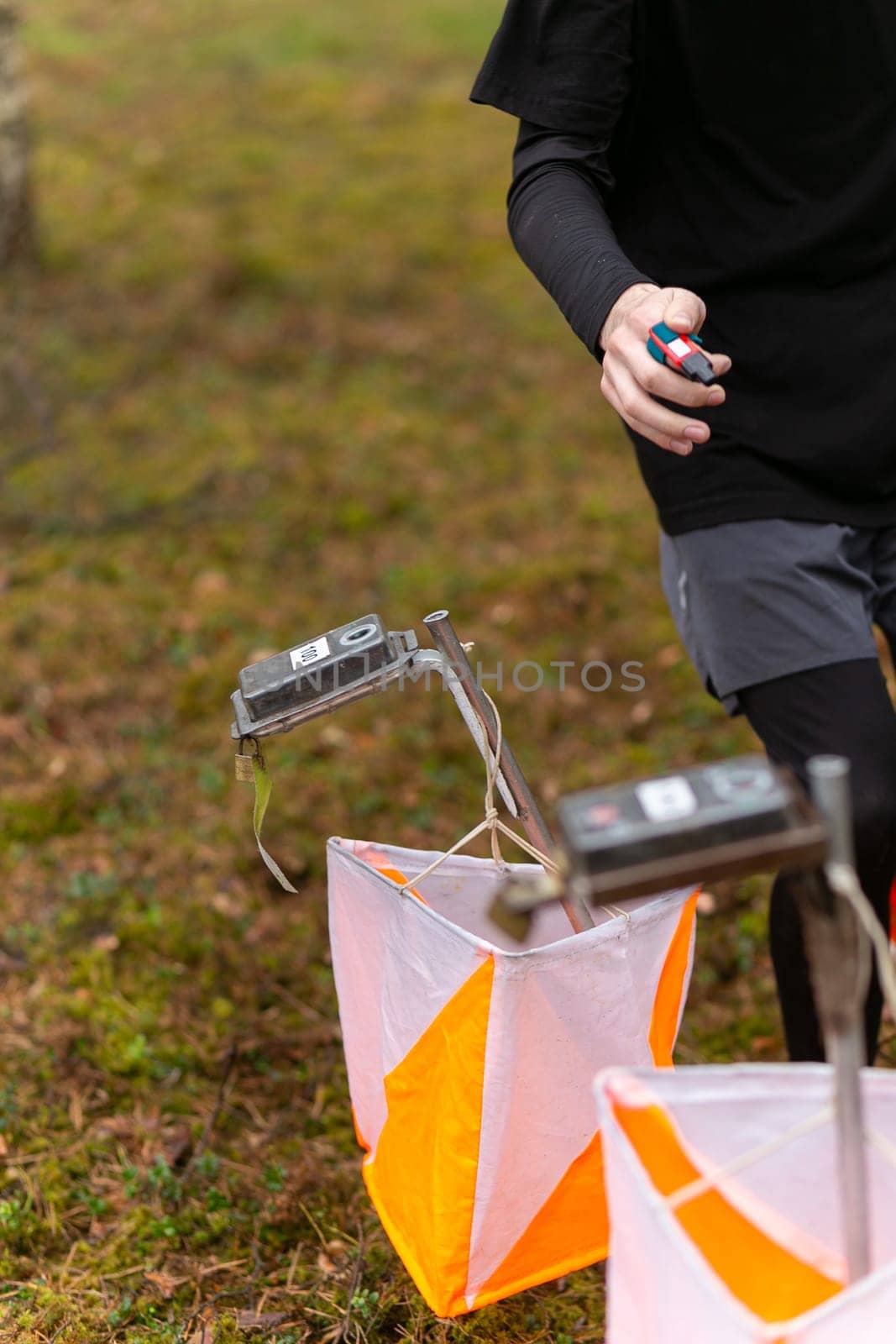 A boy punching at the orienteering control point close up. Boy in forest checking to a control point. Selective focus