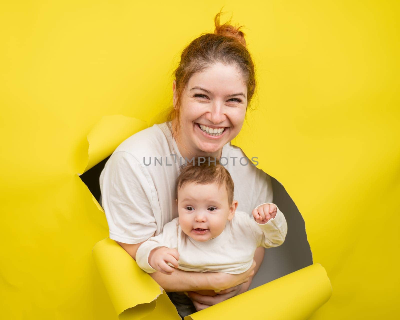 Cheerful Caucasian woman with little son rips and leans out through yellow cardboard background. by mrwed54