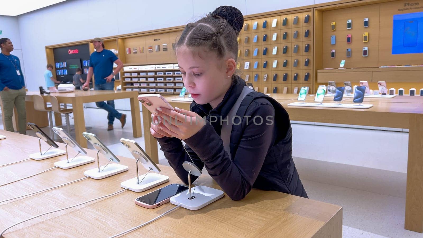 Denver, Colorado, USA-March 23, 2024-curious little girl examines the latest iPhone models on display at the Apple Store located in Park Meadows Mall, showcasing a youthful interest in technology.