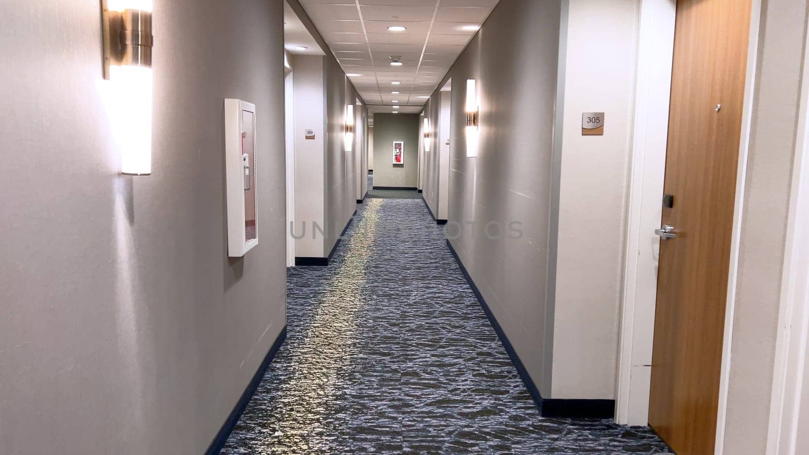 Ft Collins, Colorado, USA-March 23, 2024-A well-lit hallway stretches into the distance in a modern hotel, featuring elegant carpeting, clean lines, and a series of numbered doors on either side.