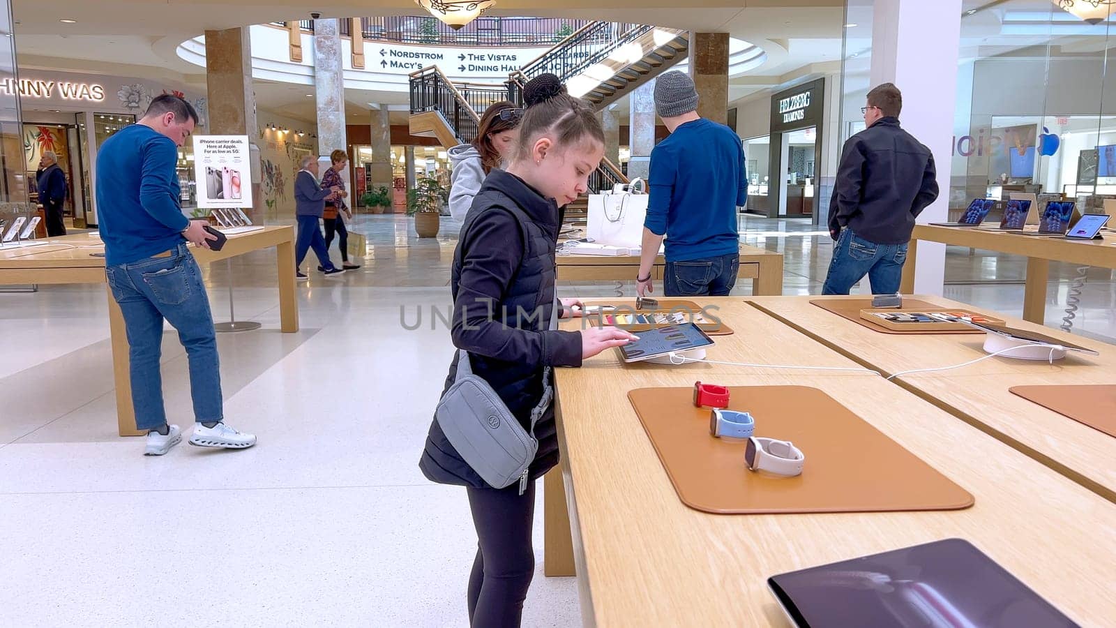 Denver, Colorado, USA-March 23, 2024-curious little girl examines the latest iPhone models on display at the Apple Store located in Park Meadows Mall, showcasing a youthful interest in technology.