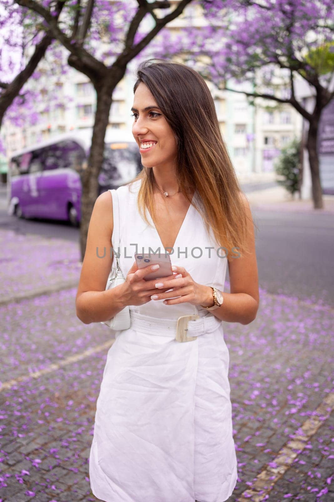 Happy woman holding smartphone near Jacaranda trees in city by andreonegin