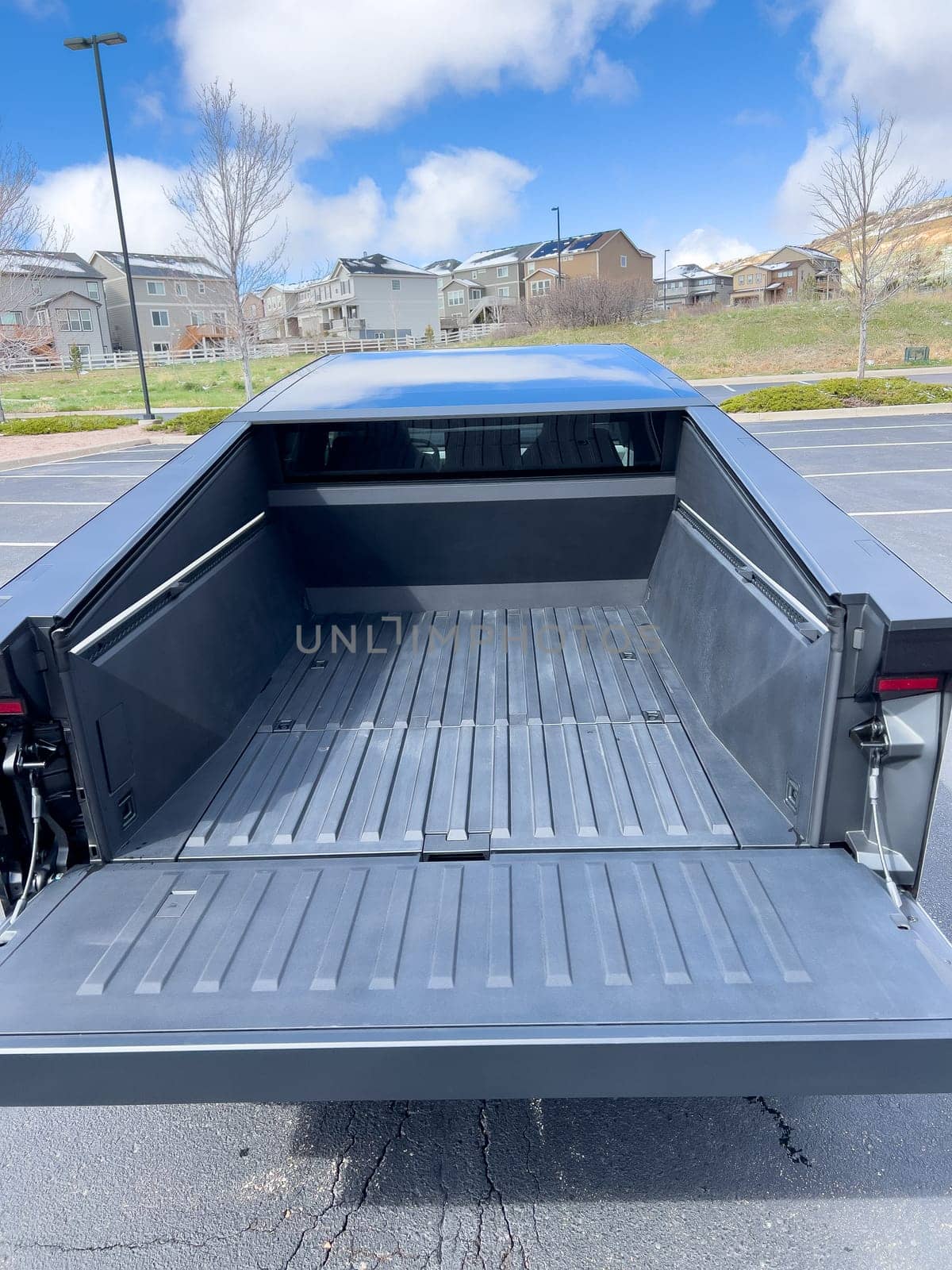 Denver, Colorado, USA-March 28, 2024-The distinctive rear end of a Tesla Cybertruck, captured in an empty parking lot, stands out against a backdrop of suburban homes under a blue sky with fluffy clouds.