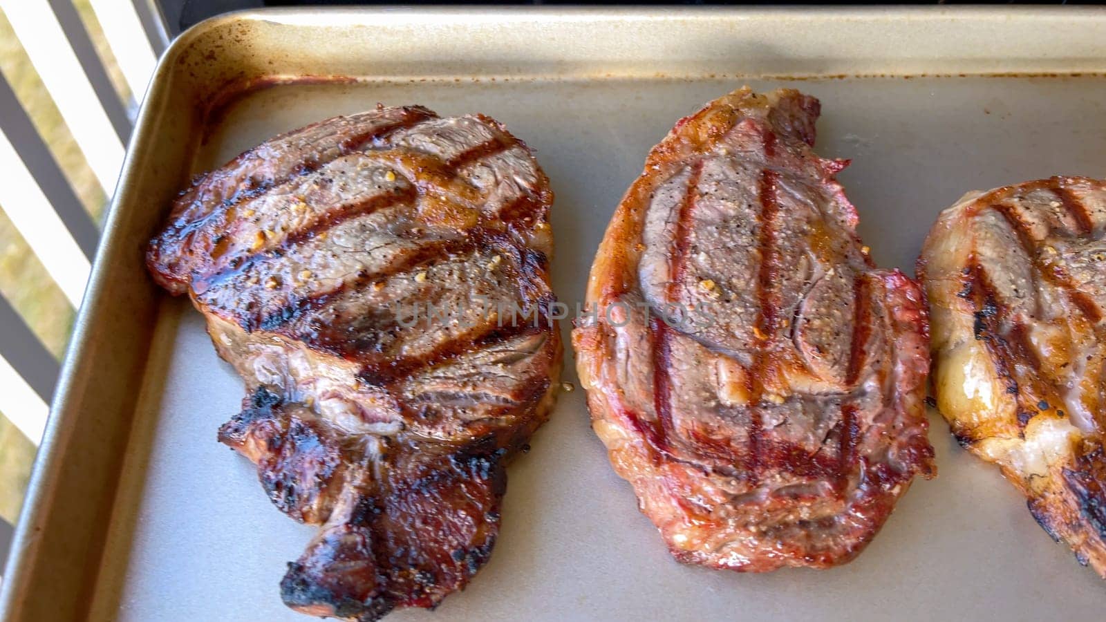 Three succulent ribeye steaks display perfect grill marks after being cooked, presented on a neutral surface, embodying the art of grilling.