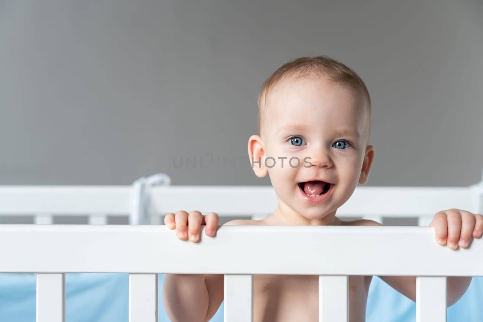 A baby laughing out loud reaches out from his crib with his hand.