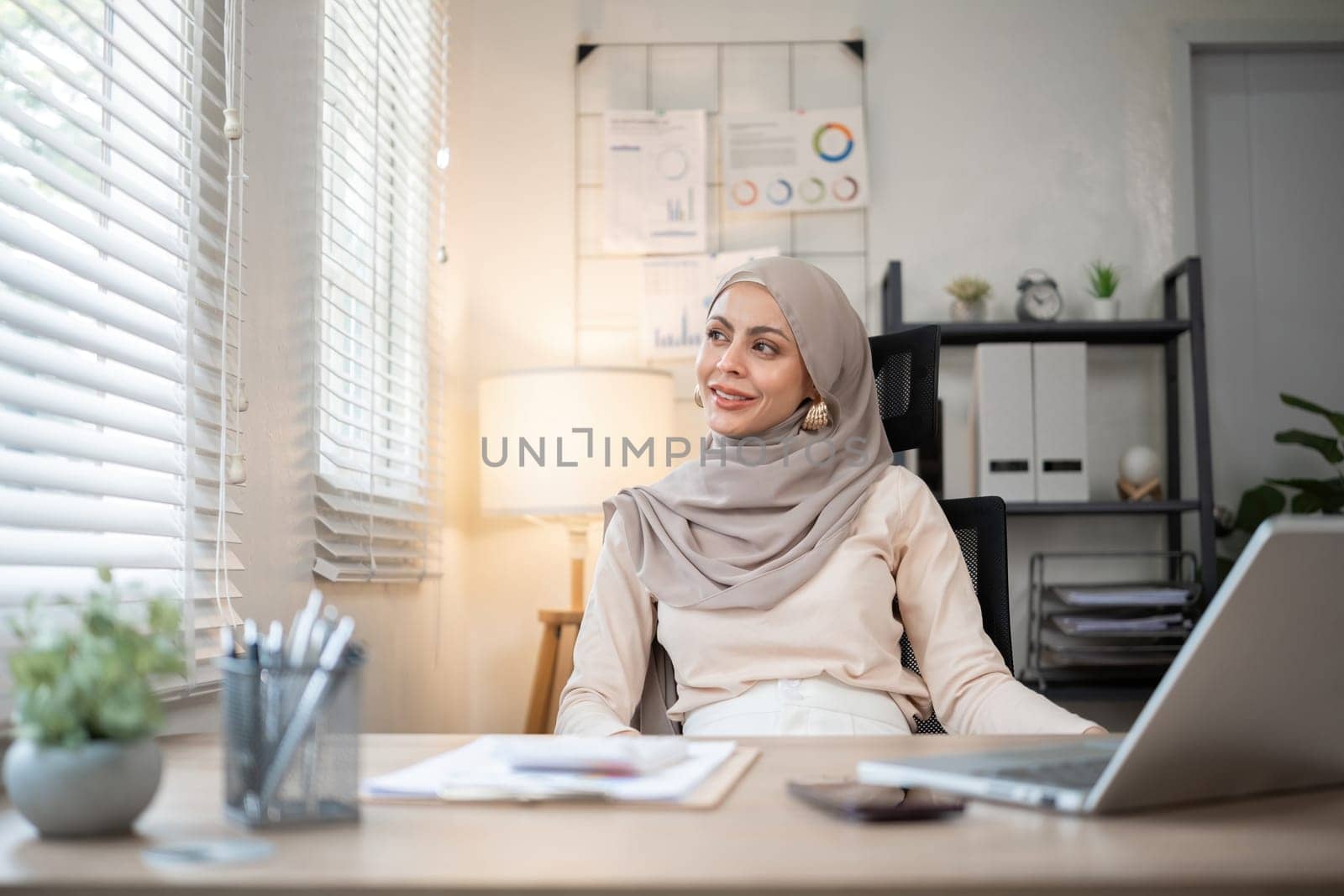 Muslim businesswoman working using laptop and taking notes on documents In the modern office by wichayada