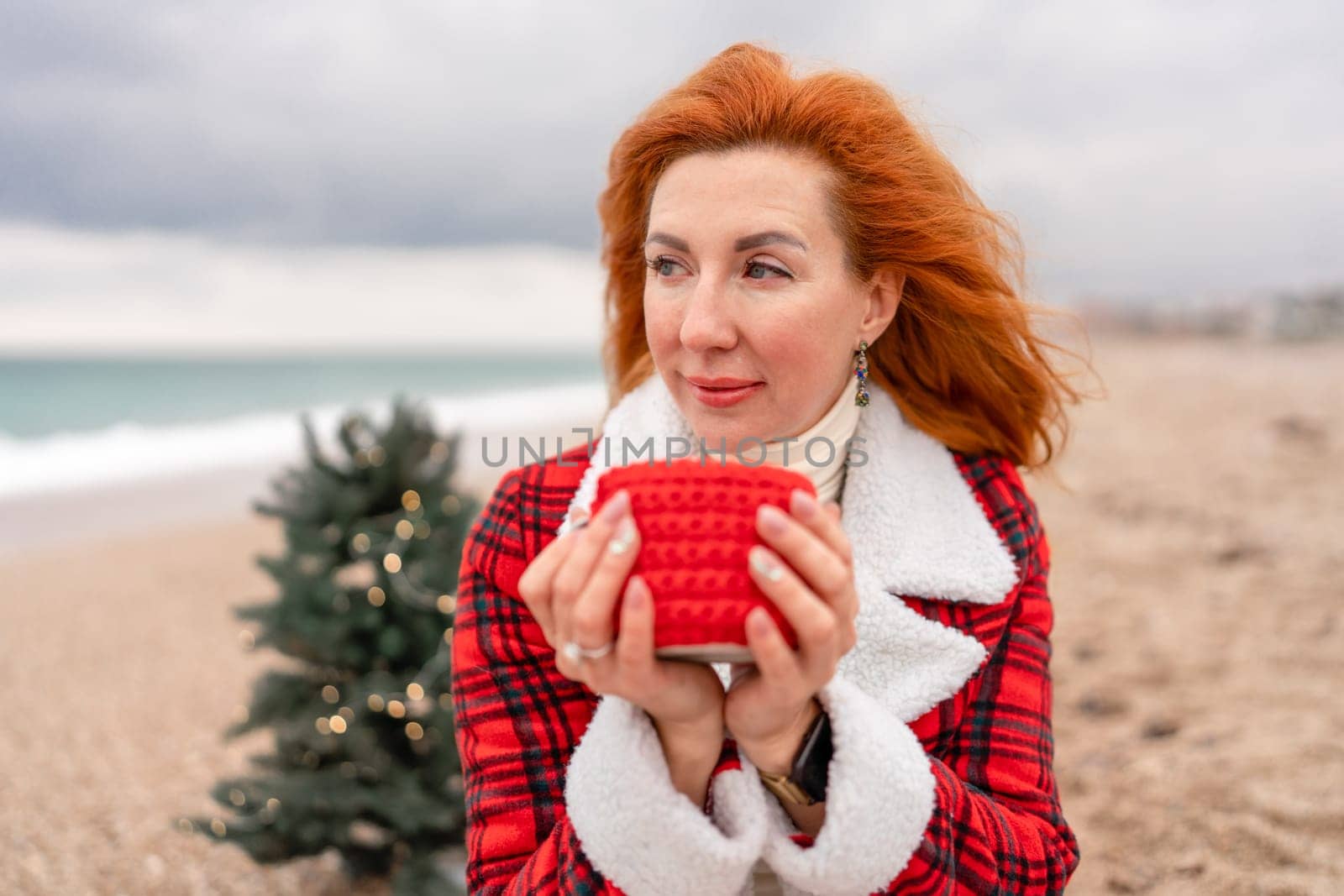 Lady in plaid shirt with a red mug in her hands enjoys beach with Christmas tree. Coastal area. Christmas, New Year holidays concep.