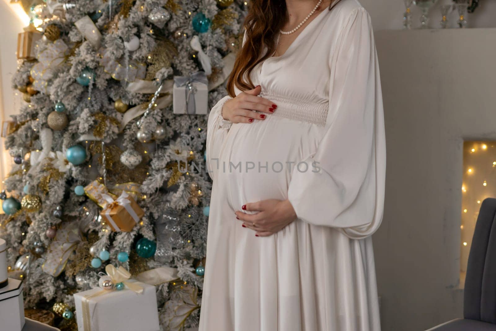 Pregnant woman holding a belly against Christmas tree with lights. family holiday concept. by Matiunina